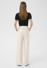 Beige wide-leg trousers with a high waist, tailored fit, and back pockets. Paired with a plain black T-shirt and minimalistic design.