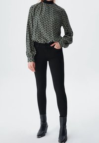 Blusa a maniche lunghe con colletto alto in un motivo a onde nero e crema, abbinata a jeans skinny neri e stivali alla caviglia. Texture liscia nel complesso.