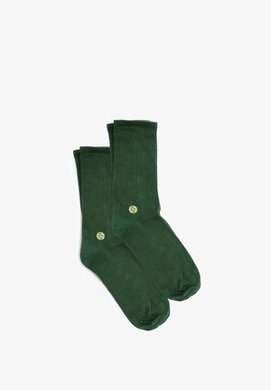 Calcetines verdes con textura de canalé, hechos de tela suave. Entre sus características se incluyen una puntera reforzada y un pequeño logo amarillo en el lateral. Longitud uniforme.