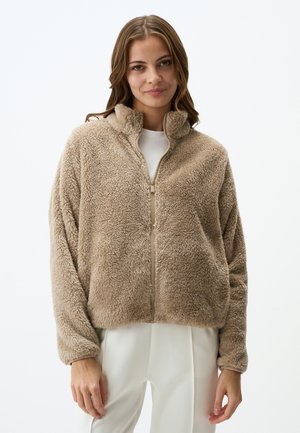 Veste zippée beige floue avec un col montant, des manches longues et une texture douce, présentant un léger éclat et sans motifs ni embellissements visibles.