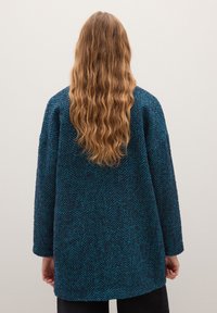 Cappotto a motivo spina di pesce in verde scuro e blu navy. Vestibilità ampia, maniche lunghe, tessuto a base di lana testurizzata, orlo arrotondato e tasche laterali.