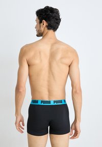 Schwarze Boxershorts mit einem hellblauen Elastikbund, der mit dem "PUMA"-Logo versehen ist. Glatte Textur, enganliegendes Design und kurze Beinlänge.