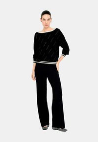 Maglione nero lavorato a maglia con strisce bianche diagonali, ampio scollo a barca e orlo a coste. Abbinate a pantaloni neri a gamba larga e scarpe basse.