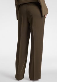 Pantaloni larghi color verde oliva scuro con una texture liscia, vita elasticizzata e tasche laterali, mostrati da dietro.