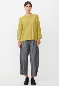 Geel gebreide trui met brede mouwen, gecombineerd met grijze wijduitlopende broek met krijtstreepjes en zwarte instapschoenen. Eenvoudig ontwerp, comfortabele pasvorm.