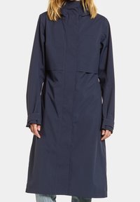 Trench-coat imperméable bleu marine avec un col haut, rabat avant, manches longues et silhouette droite. Caractérisé par des lignes épurées et peu de détails.