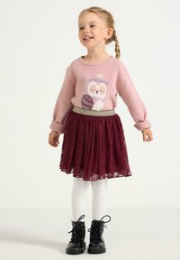 Maglione rosa chiaro con design di gufo, gonna in pizzo bordeaux, collant bianchi a fantasia e stivaletti neri con lacci. Outfit testurizzato e giocoso per bambini.