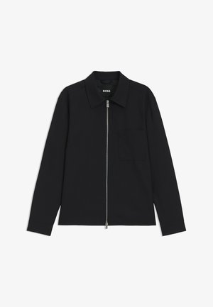 Chemise noire à manches longues avec fermeture éclair sur le devant, col plat, poche sur la poitrine gauche et tissu texturé. Design simple sans motifs ni accents visibles.