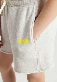 Pelēki kokvilnas šorti ar sakostu apakšmalu, sānu kabatām un dzeltenu "American Vintage" logotipu. Audums ir mīksts un ar teksturētu izskatu.