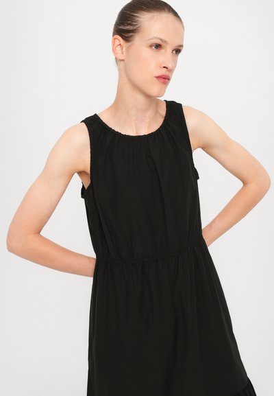 Black dress made of lightweight fabric; features a round neck, sleeveless design, elastic waist, and a flowing skirt with a ruffled hem.