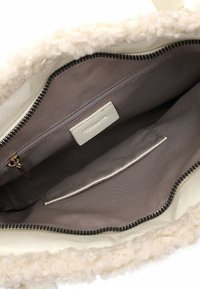 Vnitřek tašky v barvě smetany s šedou látkovou podšívkou, jednou kapsou na zip se zlatým táhlem a jednou otevřenou kapsou, vše uvnitř otvoru s kudrnatým lemováním.