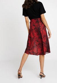 Röd och svart ormtryckt midikjol med en flödande silhuett och lättviktig tyg. Har hög midja och en design med slits bak.