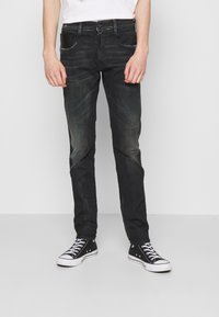 Jeans negros de denim, con un ajuste slim, textura desgastada, cinco bolsillos y cierre de botón. Combinados con zapatillas de lona negras.