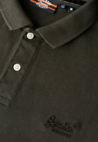 Mørkegrøn polo-shirt med et struktureret stof. Har en klassisk krave, tre-knaps lukning og broderet logo på brystet.