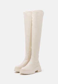 Knee-high white boots featuring a smooth, glossy finish, textured rubber soles, side zipper, and chunky platform design.