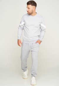 Helles graues Sweatshirt mit weißen Akzenten und passenden Jogginghosen, aus weichem Stoff hergestellt, mit gerippten Bündchen und schmal zulaufenden Knöcheln.
