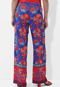 Blumenmuster-Haremshosen in Blau mit roten und türkisfarbenen Mustern, elastischem Bund und einem kontrastierenden roten Saum mit blauen Akzenten.