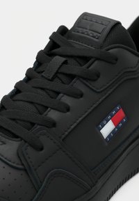 Baskets noires Tommy Jeans avec lacets, détails cousus et patch logo rouge, blanc et bleu sur le côté.