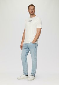 Biała bawełniana koszulka z graficznym nadrukiem, w połączeniu z jasnoniebieskimi dżinsami i białymi sneakersami. Prosty design i luźny krój.