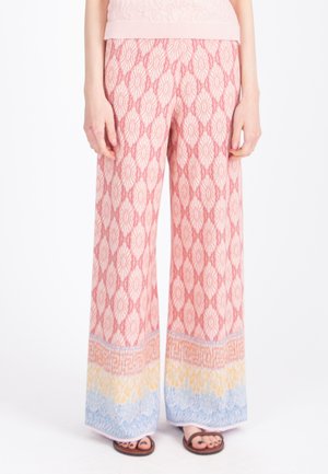 Spodnie o szerokich nogawkach z różowymi diamentowymi wzorami i wielokolorowymi paskami przy krawędzi, zestawione z brązowymi sandałami z odkrytymi palcami i ciemnym lakierem do paznokci.