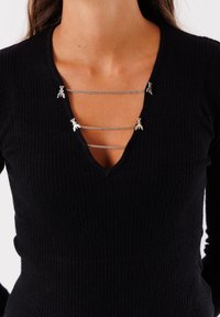 Maglione nero a coste con scollatura a V profonda, impreziosito da catene argentate decorate con piccoli accenti lungo il collo.