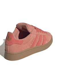 Une paire de baskets Adidas en daim rose avec semelle en gomme, trois bandes sur le côté et languette de talon de marque, vue de l'arrière en angle latéral.