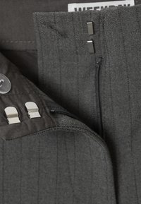Tissu gris avec un motif à rayures verticales comportant une fermeture éclair, des accents en métal et une étiquette tissée. Texture lisse.