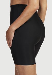 Svarta högmidjade formande shorts i mjukt och elastiskt material; har en sömlös design och slutar vid mitten av låret.