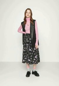 Saia preta com padrões florais e detalhes em roxo, combinada com um suéter de gola alta rosa e um colete de pele preto. Completo com sapatos pretos e meias claras.