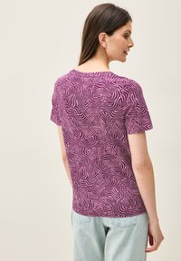 Camiseta de manga corta morada con un patrón blanco ondulado, fabricada en tejido suave, con un cuello redondo y un corte relajado.