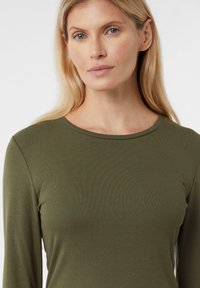 Oliwkowo-zielona bluzka z długim rękawem i okrągłym dekoltem, wykonana z prążkowanej tkaniny. Gładka faktura, dopasowany krój, bez widocznych wzorów czy akcentów.