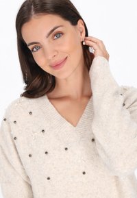 Fény bézs kötött pulóver V-kivágással, ezüst és fekete gyöngyökkel díszítve, valamint finom virágmintákkal az elején.