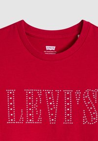 Punane puuvillane T-särk ümaratest kaelustest, mille esiküljel on hõbedast strassidega "LEVI'S" logo. Sildid on kaeluses.