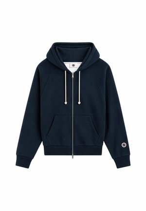 Sudadera con capucha azul marino con cremallera, bolsillos delanteros, cordones blancos, puños acanalados y un pequeño parche circular en el puño de la manga izquierda.