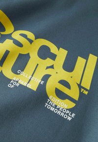 Zeleni materijal s velikim žutim i bijelim tekstom. Dizajn uključuje "SKULPTURNA KOLEKTIVA OBUĆA ZA IZLAGANJE LJUDIMA SUTRA."