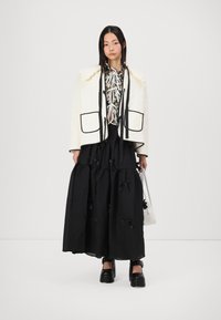 Κουβερτίνα λευκή με μαύρες λεπτομέρειες και τσέπες, συνδυασμένη με μαύρη φούστα με tiered σχέδιο και φιόγκους, καθώς και μαύρα πλατφόρμα παπούτσια.