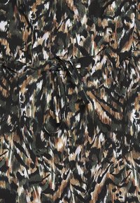 Tissu avec un motif camouflage abstrait vert, marron, noir et blanc, doté d'un cordon de serrage noué avec des embouts métalliques.