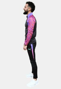 Chándal deportivo con un cuerpo gris y mangas con un diseño vibrante en rosa y púrpura, combinado con pantalones negros con rayas rosas. Zapatillas blancas.