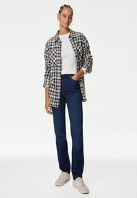 Kollad flanellskjorta i svart och vitt över en vit ribbad t-shirt. Blå jeans och beige sneakers kompletterar outfiten.