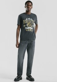 Czarny t-shirt z grafiką lwa i napisem, zestawiony z ciemnymi dżinsami i czarnymi masywnymi butami. Gładka tkanina, casualowy krój.