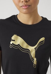 Tricou negru din bumbac, cu un mare logo auriu Puma, cu un design stratificat, plasat în centrul frontal. Mâneci scurte și gât rotund.