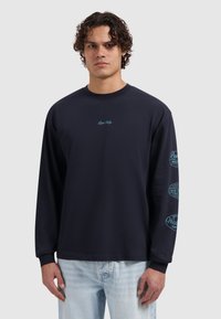 Marineblauw t-shirt met lange mouwen van katoen, met lichtblauwe logo's op de voorkant en mouwen, een ronde hals en een standaard pasvorm. Casual ontwerp.