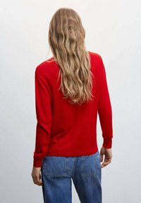 Rode gebreide trui met lange mouwen, geribbelde manchetten en een ronde hals, gecombineerd met blauwe jeans. Soepele textuur, aansluitend ontwerp.