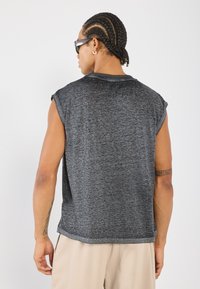 Gray sleeveless top with a soft, textured fabric, rounded neckline, and loose fit, featuring a stitching detail at the shoulder seams.