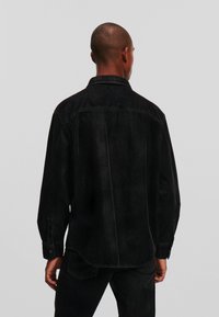 Cămașă din denim negru cu mâneci lungi, manșete cu nasturi și color. Are cusături întunecate și o textură ușor estompată pe spate.