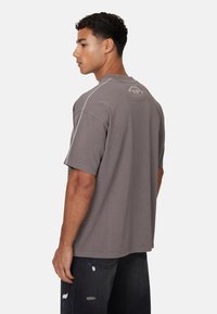 Grijze oversized t-shirt met een ronde halslijn, korte mouwen en een logo-detail aan de achterkant. Materiaal lijkt zacht met subtiele stiksels.