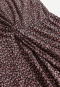 Tissu noir avec un petit motif floral rose et blanc, rassemblé en un nœud central créant de doux plis.