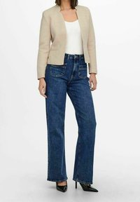 Blazer beige sur un haut blanc, assorti à un jean droit taille haute bleu foncé. Talons noirs complètent la tenue.