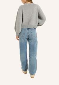 Grauer Strickpullover mit verkürzter Passform und geripptem Saum, kombiniert mit hellblauen, hoch sitzenden Jeans mit Gesäßtaschen und geradem Bein.