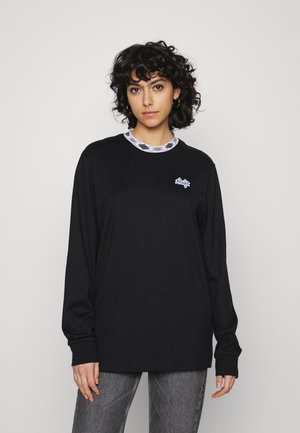 Camisa de mangas longas preta com decote redondo e logótipo gráfico em branco no peito. Por baixo, um colarinho estampado em preto e branco.